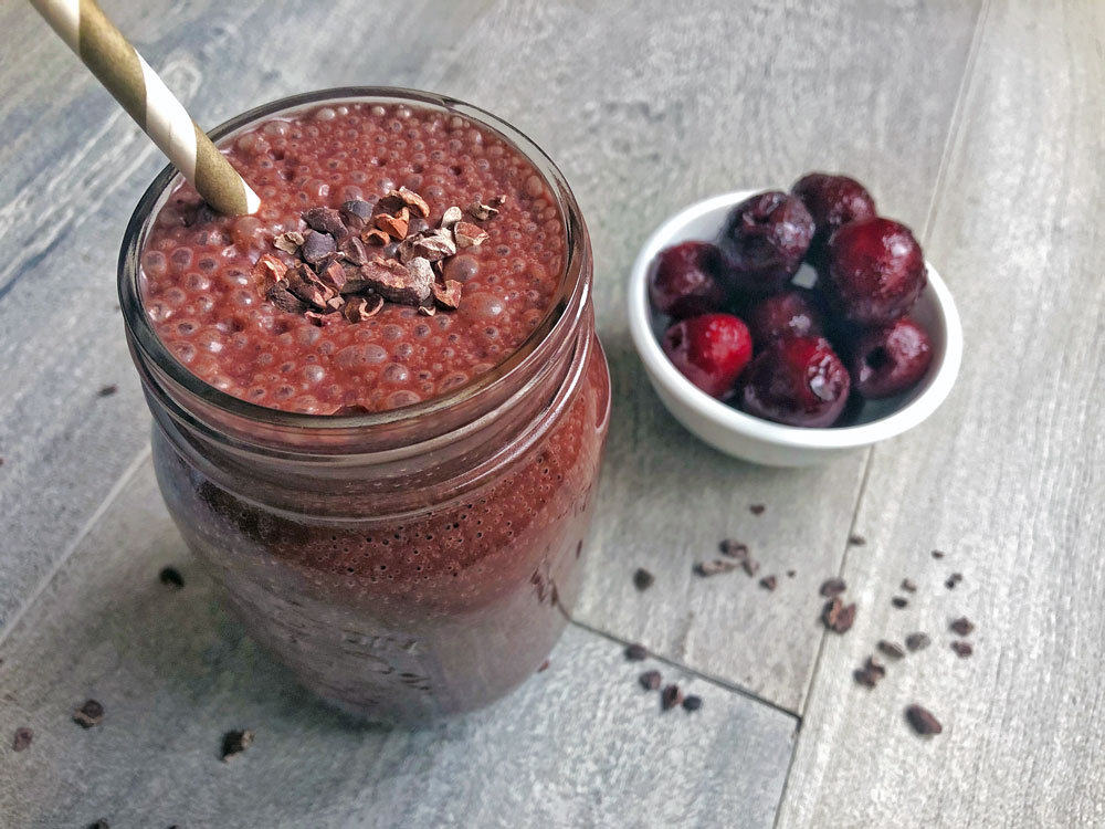 Warm chocolate cherry smoothie in a mason jar on a grey table with bowl of cherries.