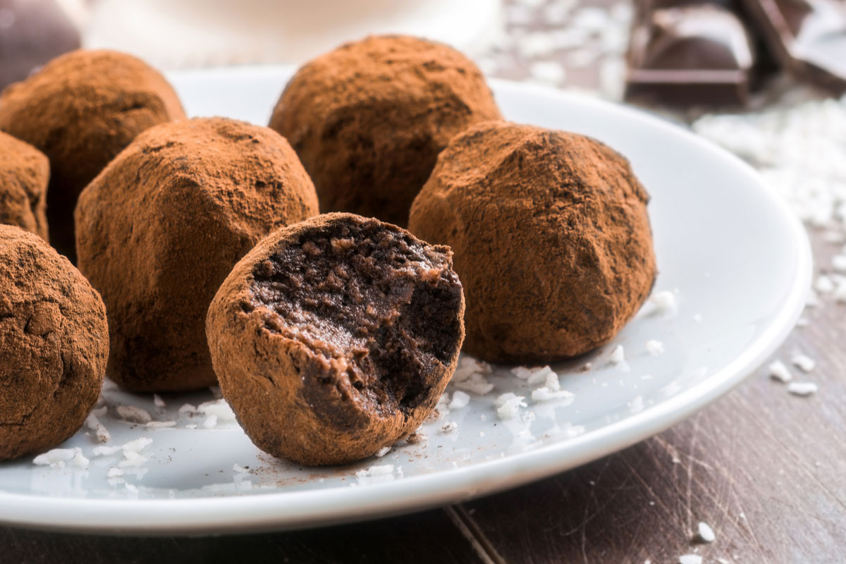 Raw chocolate avocado truffles on a white plate with coconut flakes.