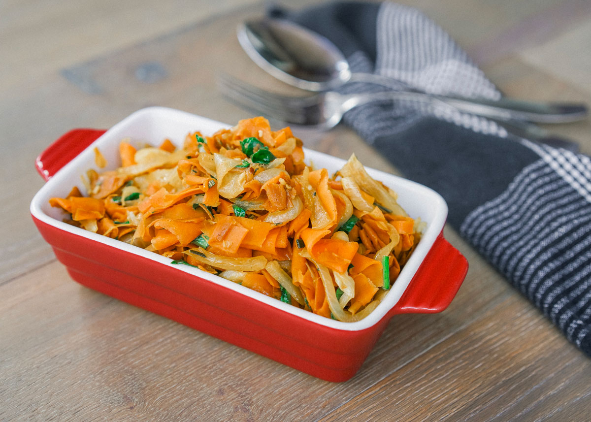 Rosemary honey carrot ribbons in a red dish with black towel in the background.